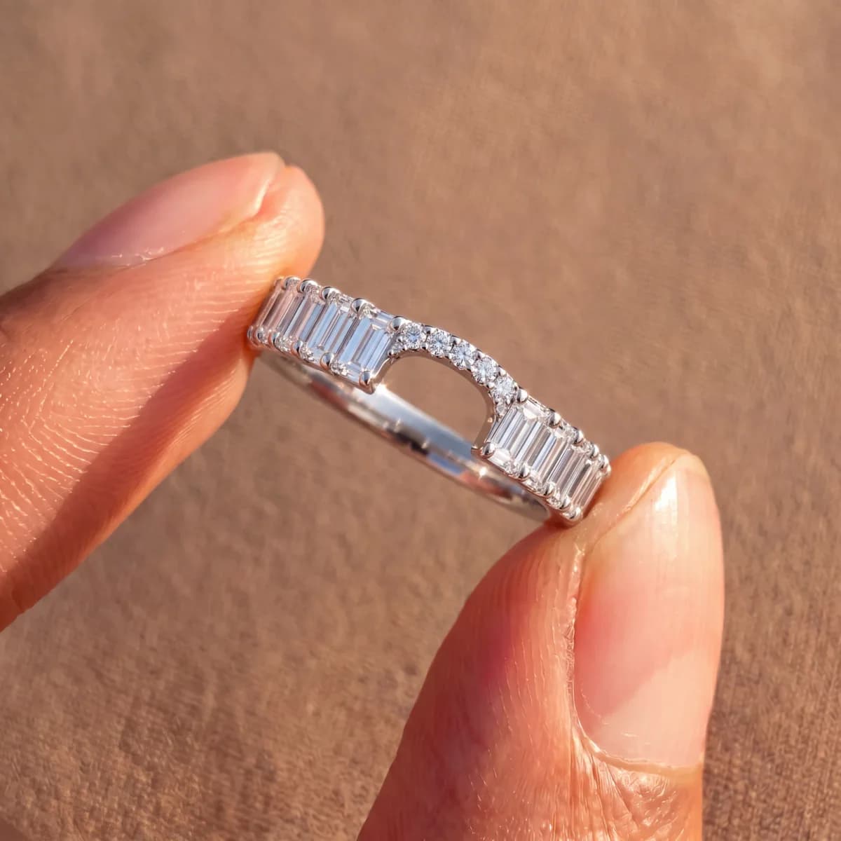 The same curved diamond band held between a thumb and forefinger, which shows its size against the hand